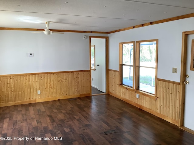 spare room featuring visible vents, a ceiling fan, dark wood-style floors, wooden walls, and a wainscoted wall