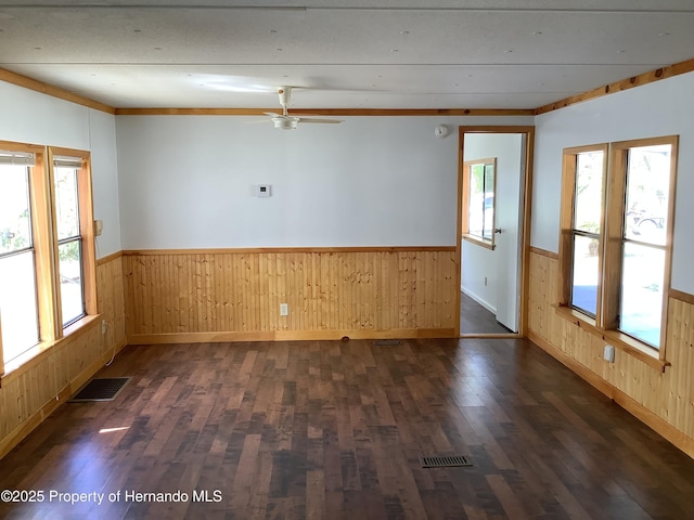 unfurnished room featuring wooden walls, visible vents, and wainscoting