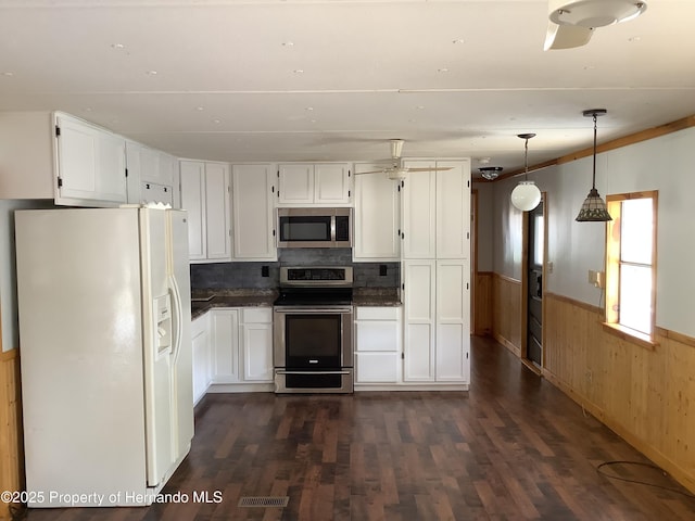 kitchen with white cabinetry, a wainscoted wall, wood walls, dark wood-type flooring, and appliances with stainless steel finishes