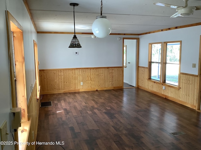 empty room featuring dark wood-type flooring, wainscoting, visible vents, and wooden walls