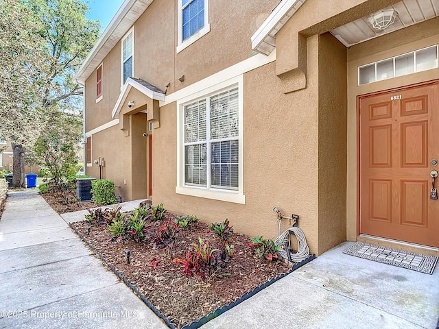 view of exterior entry with cooling unit and stucco siding