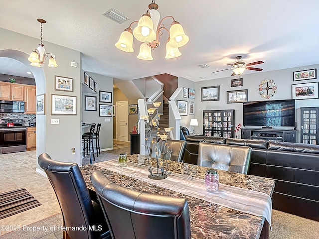 dining area with arched walkways, stairway, visible vents, and ceiling fan with notable chandelier