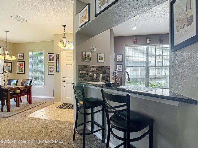 kitchen featuring tasteful backsplash, a textured ceiling, an inviting chandelier, and visible vents