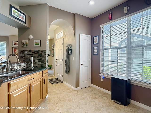 kitchen with arched walkways, tasteful backsplash, a sink, dark countertops, and baseboards