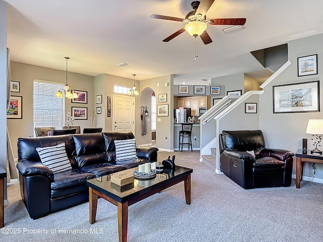 carpeted living area with baseboards, stairs, visible vents, ceiling fan, and arched walkways