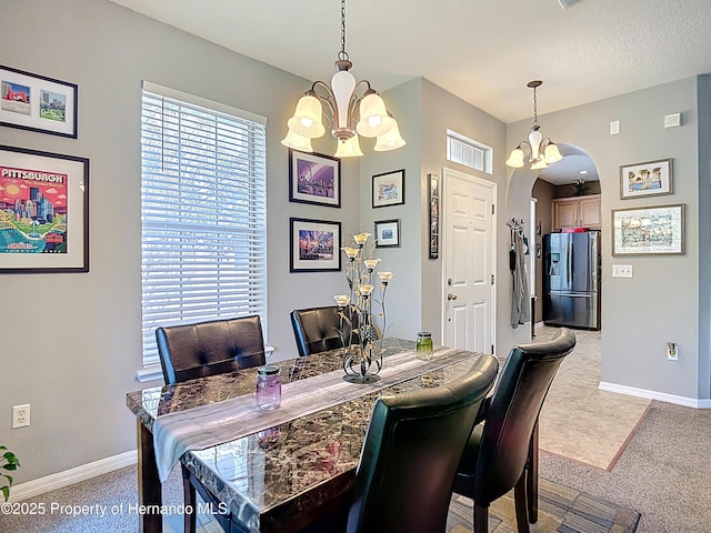 carpeted dining area featuring a chandelier, arched walkways, and baseboards