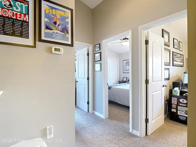 hallway featuring carpet flooring, baseboards, and vaulted ceiling