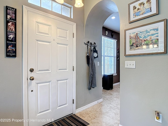 foyer with arched walkways, light tile patterned floors, plenty of natural light, and baseboards