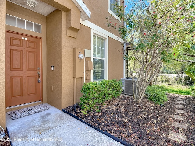 property entrance featuring cooling unit, stucco siding, and fence