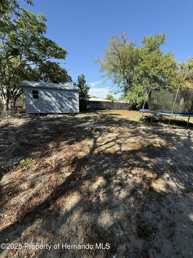 view of yard with an outbuilding, fence, a trampoline, and a storage shed