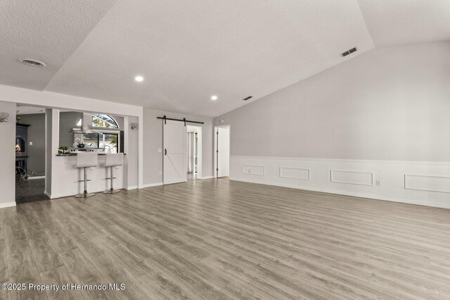 4405 Plumosa St, Spring Hill, FL 34607 - unfurnished living room with a barn door, wood finished floors, wainscoting, lofted ceiling, and visible vents