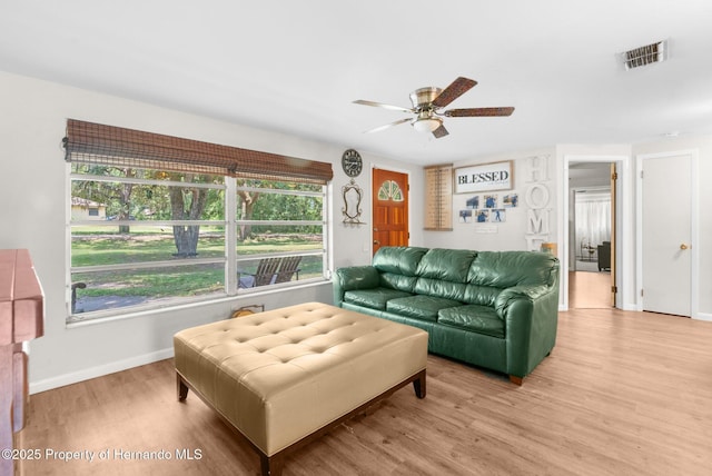 living room with light wood-style floors, visible vents, baseboards, and ceiling fan