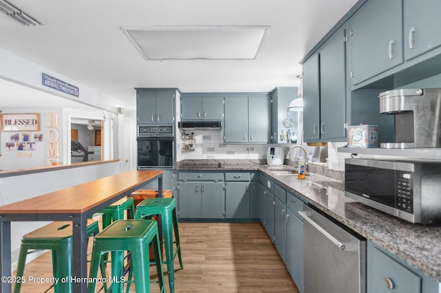 kitchen featuring stainless steel appliances, a sink, visible vents, wood finished floors, and under cabinet range hood
