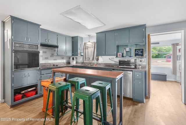 kitchen with backsplash, under cabinet range hood, light wood-style floors, and black appliances
