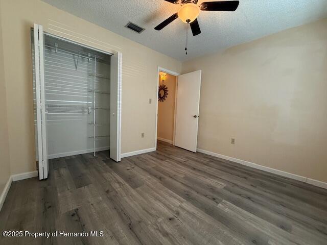 947 Village Dr, Brooksville, FL 34601 - unfurnished bedroom featuring wood finished floors, baseboards, a textured ceiling, a closet, and ceiling fan