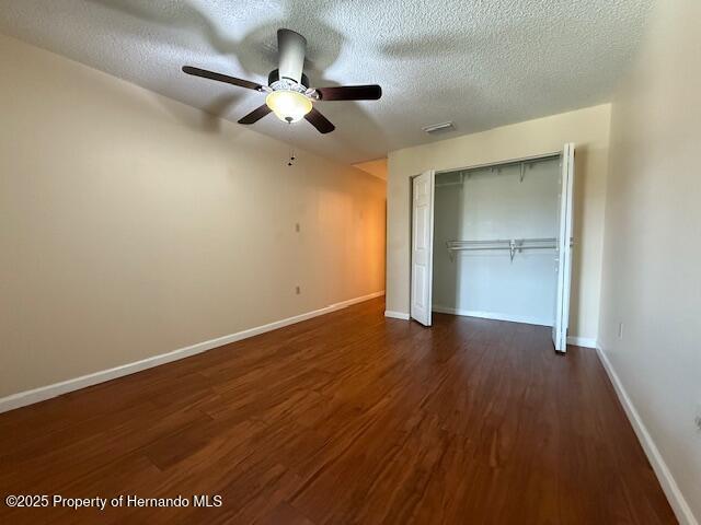 947 Village Dr, Brooksville, FL 34601 - unfurnished bedroom featuring dark wood-type flooring, baseboards, a textured ceiling, a closet, and ceiling fan