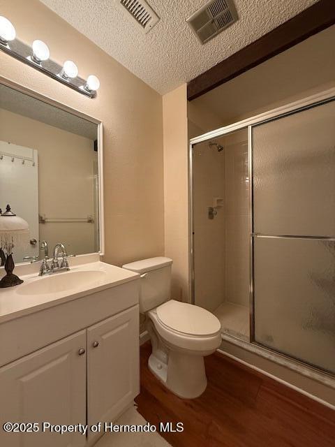 947 Village Dr, Brooksville, FL 34601 - bathroom with wood finished floors, a shower stall, a textured ceiling, toilet, and vanity