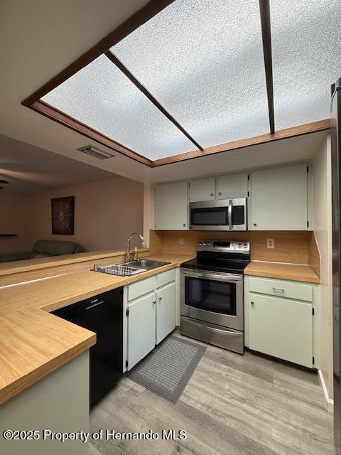 947 Village Dr, Brooksville, FL 34601 - kitchen featuring appliances with stainless steel finishes, a sink, light wood-style floors, a peninsula, and butcher block counters