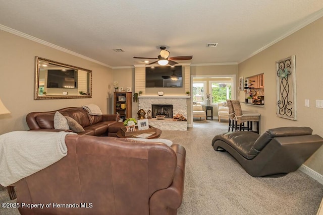 carpeted living room with a stone fireplace, ornamental molding, baseboards, and ceiling fan