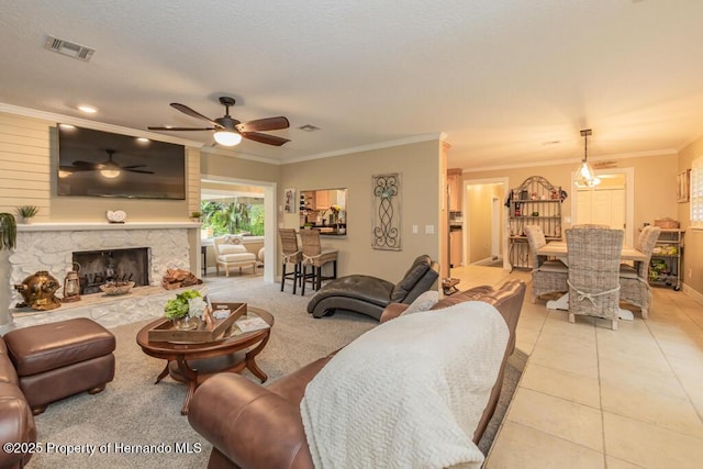 living area with visible vents, ornamental molding, ceiling fan, a stone fireplace, and light tile patterned floors