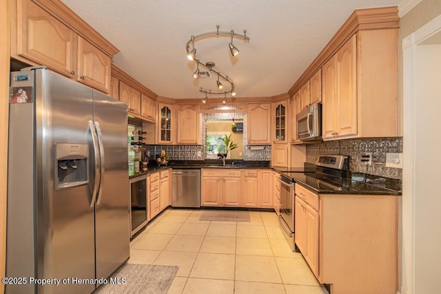 kitchen with tasteful backsplash, a sink, light tile patterned flooring, glass insert cabinets, and appliances with stainless steel finishes