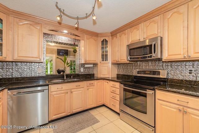 kitchen with stainless steel appliances, light brown cabinetry, a sink, glass insert cabinets, and light tile patterned floors