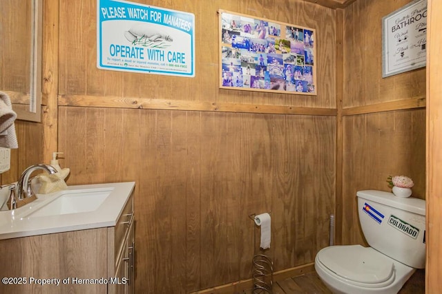 half bathroom featuring wood walls, vanity, and toilet