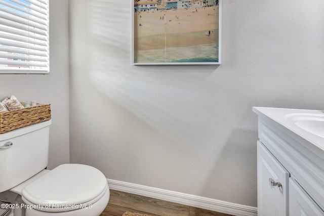 bathroom with toilet, wood finished floors, vanity, and baseboards