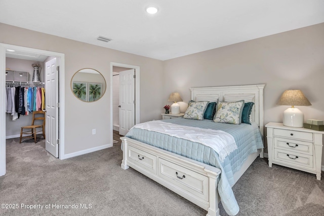 bedroom with visible vents, a closet, baseboards, light carpet, and a walk in closet