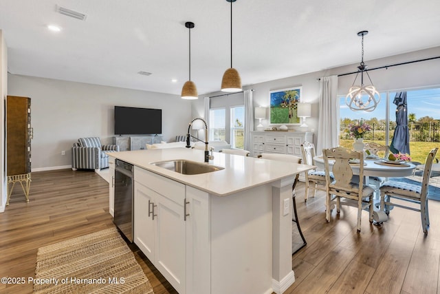 kitchen with wood finished floors, stainless steel dishwasher, a chandelier, a sink, and open floor plan