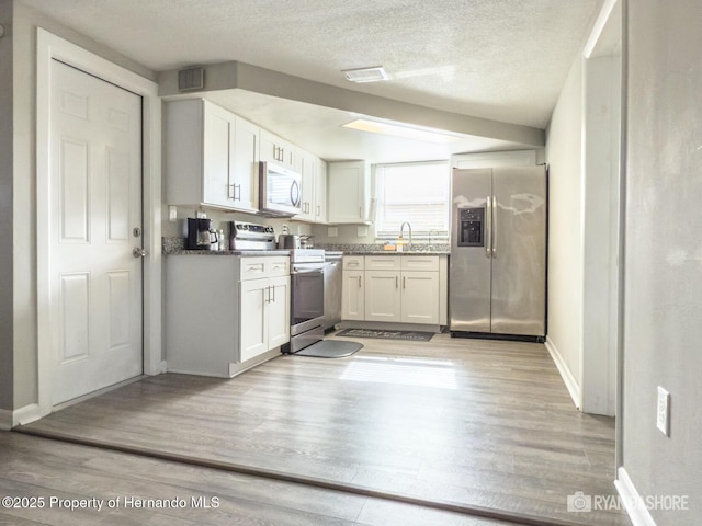 kitchen featuring light wood-style floors, appliances with stainless steel finishes, baseboards, white cabinetry, and visible vents