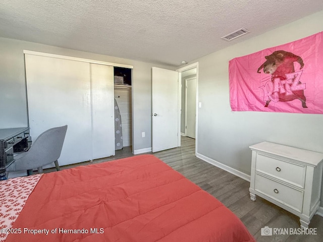 bedroom with a textured ceiling, baseboards, visible vents, wood finished floors, and a closet