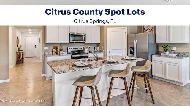 kitchen with a kitchen breakfast bar, a sink, a kitchen island with sink, light tile patterned floors, and stainless steel appliances