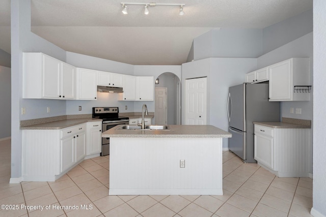 kitchen featuring stainless steel appliances, a sink, under cabinet range hood, vaulted ceiling, and arched walkways