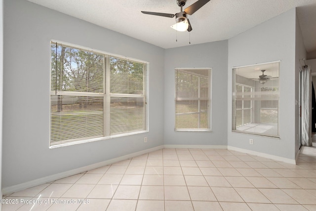 spare room featuring ceiling fan, a textured ceiling, light tile patterned floors, and baseboards
