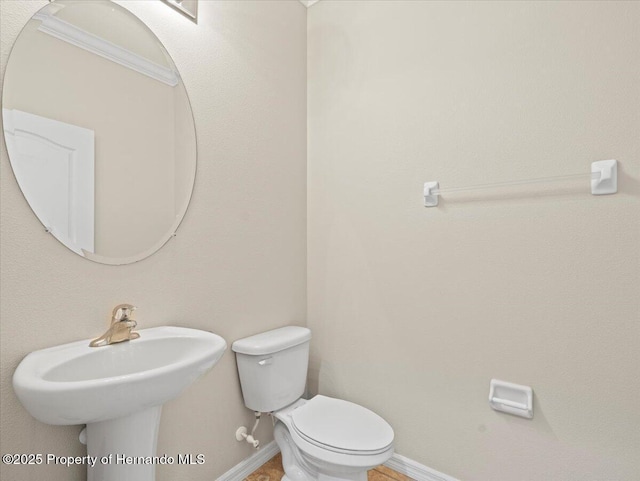 half bath featuring baseboards, toilet, and a sink
