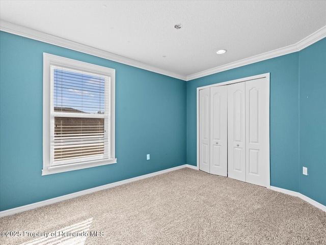 unfurnished bedroom with ornamental molding, carpet, a closet, baseboards, and a textured ceiling