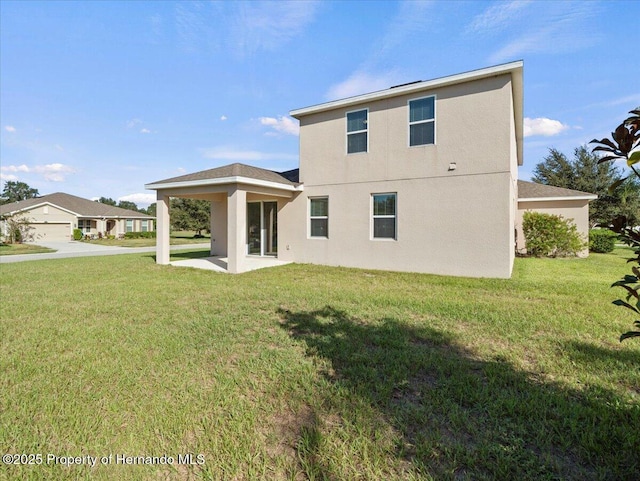 rear view of house with a lawn, stucco siding, and a patio area