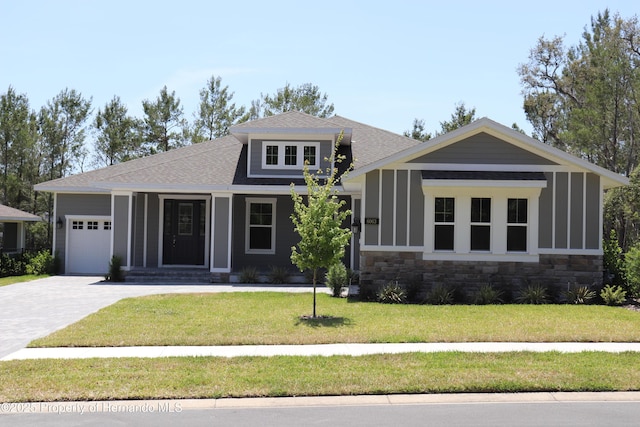 6063 Dusk Rose Ln, Brooksville, FL 34601 - view of front facade with driveway, an attached garage, stone siding, a front yard, and a shingled roof