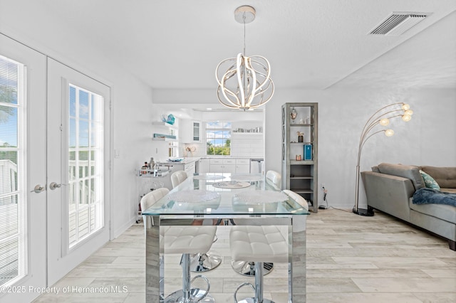 dining area featuring visible vents, light wood-style floors, baseboards, a chandelier, and french doors