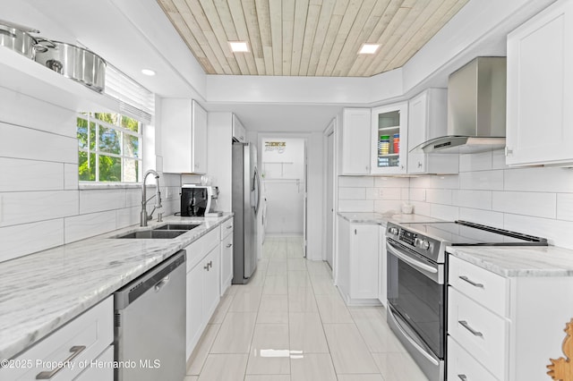 kitchen featuring tasteful backsplash, a sink, light tile patterned flooring, stainless steel appliances, and wall chimney exhaust hood