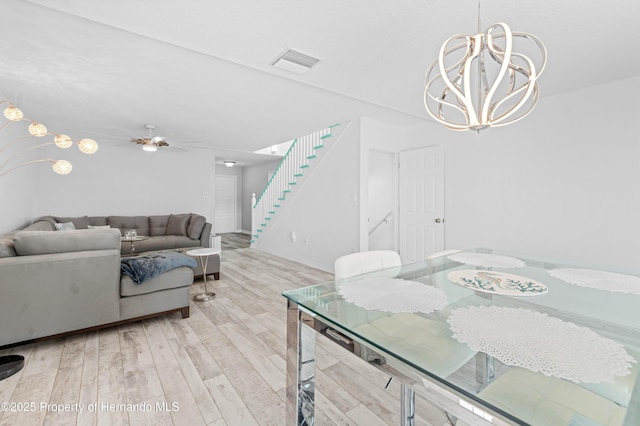 dining room with stairs, visible vents, light wood finished floors, and ceiling fan with notable chandelier