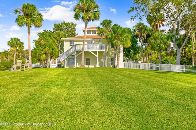 rear view of house with a lawn, a wooden deck, fence, and stairway