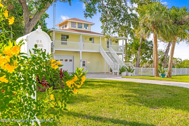 coastal inspired home featuring fence, stairs, an attached garage, a front yard, and covered porch