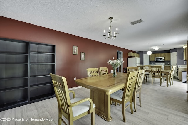 11257 Persimmon Ave, Weeki Wachee, FL 34614 - dining space with a chandelier, visible vents, light wood-style floors, and a textured ceiling