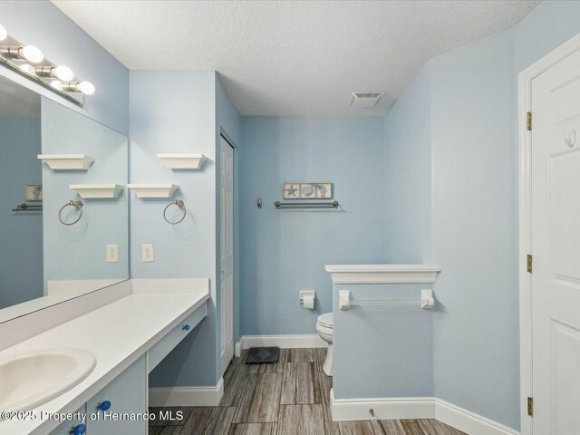 18441 Whitacre Cir, Hudson, FL 34667 - bathroom featuring wood finished floors, toilet, vanity, baseboards, and a textured ceiling