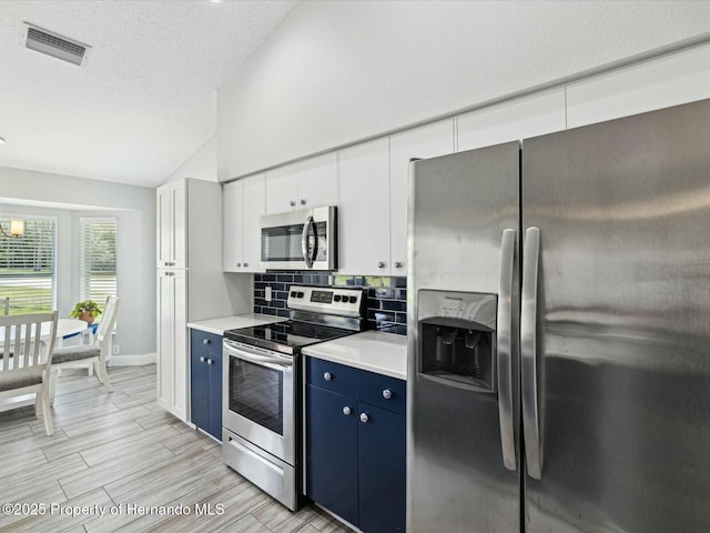 18441 Whitacre Cir, Hudson, FL 34667 - kitchen with appliances with stainless steel finishes, visible vents, vaulted ceiling, light countertops, and blue cabinets