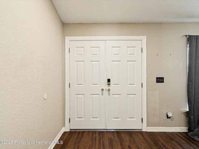 foyer featuring baseboards, dark wood finished floors, and a textured wall