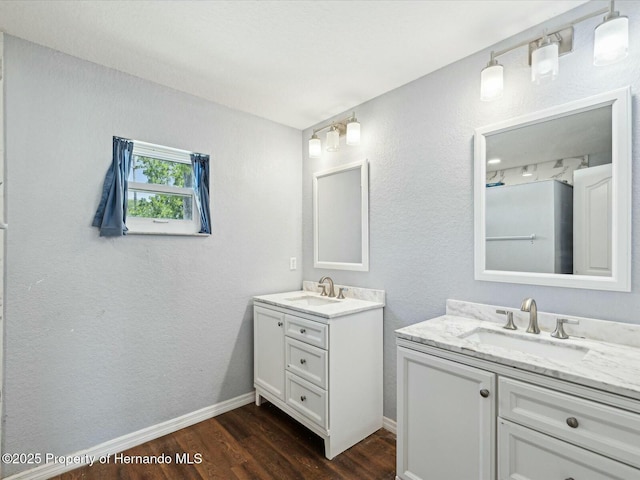full bath featuring two vanities, wood finished floors, baseboards, and a sink