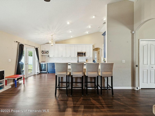 kitchen with a breakfast bar area, vaulted ceiling, white cabinets, and stainless steel microwave